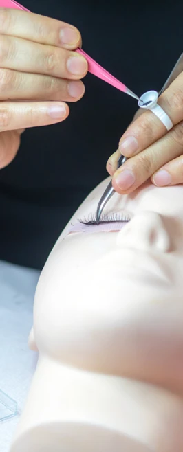 A close-up of a beauty therapy student applying eyelash extensions with tweezers to a mannequin head, focusing on precision techniques. A close-up of a beauty therapy student applying eyelash extensions with tweezers to a mannequin head, focusing on precision techniques.